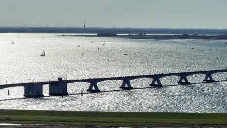 Drohnenaufnahme-Der-Zeelandbrücke-Mit-Langem-Objektiv-Und-Gegenlicht,-In-Der-Ferne-Sind-Segelboote-Zu-Sehen