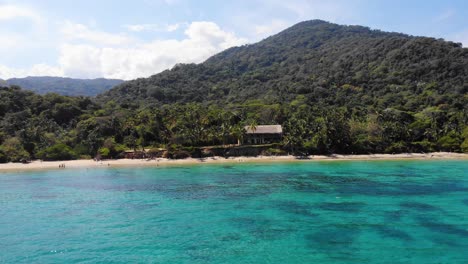 vista aérea sobre el mar poco profundo y turquesa, con vistas a una playa y la selva en la costa del parque natural nacional de tayrona, día soleado, en colombia - seguimiento, toma de avión no tripulado