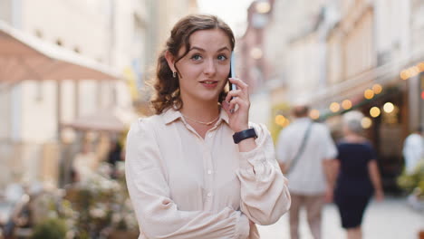 Happy-young-woman-having-remote-conversation-talking-on-smartphone,-good-news-gossip-in-city-street