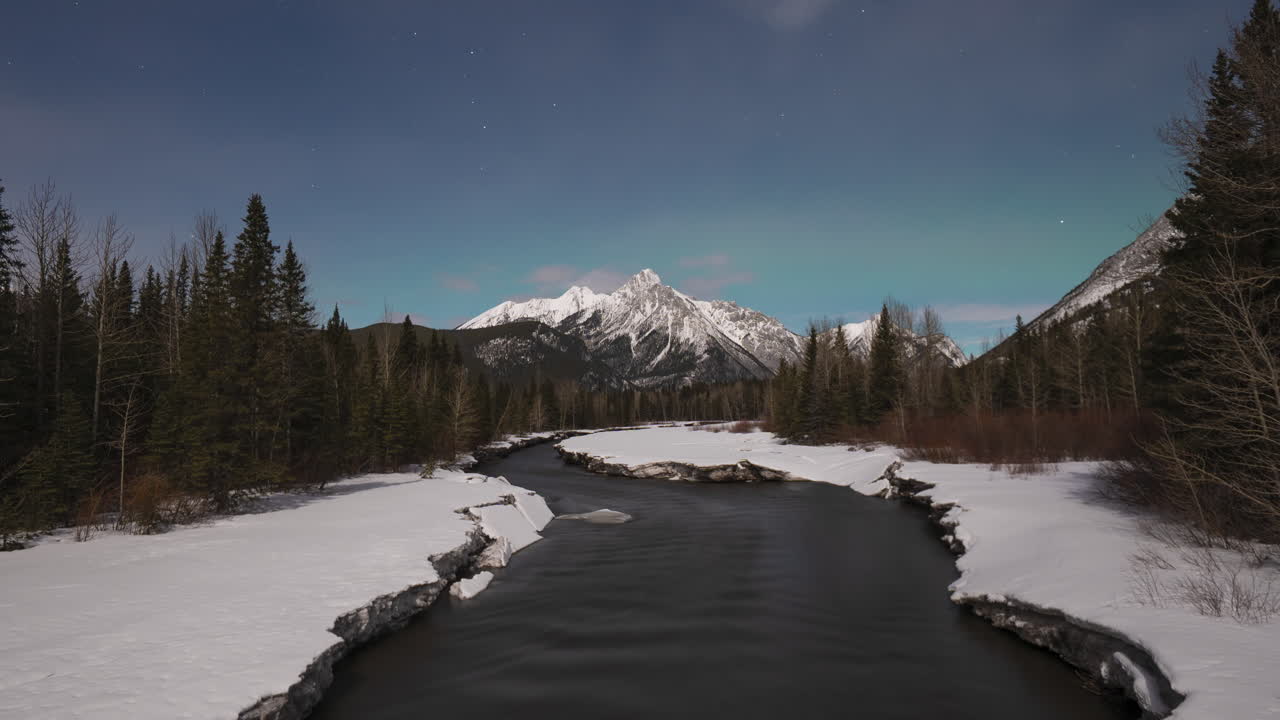 Evening timelapse of a melting river in the Canadian Rockies with northern lights appearing