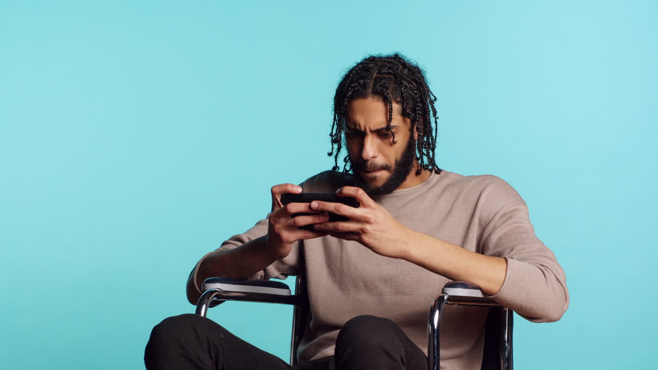 Man in wheelchair feeling sad after losing videogame, playing on mobile phone