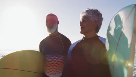 senior african american couple walking with surfboards at the beach