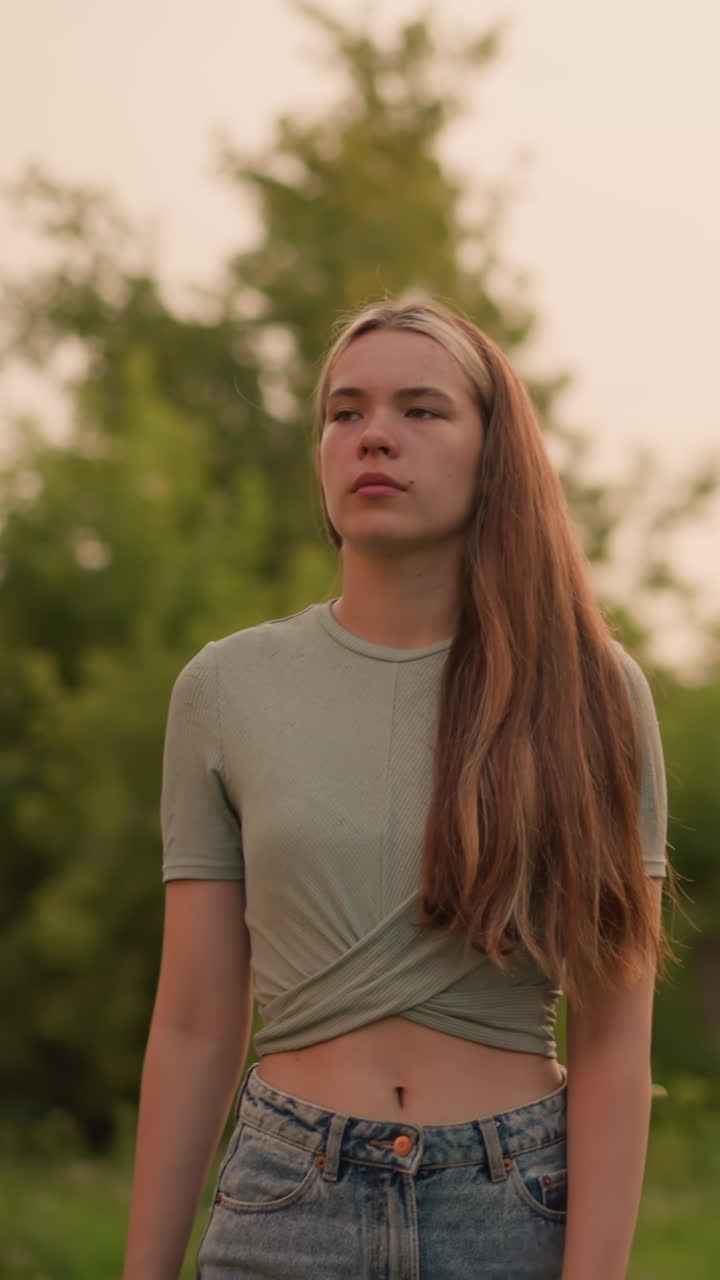 mujer joven con el cabello largo caminando por el camino de hierba, mirando cansado y contemplativo. líneas eléctricas y fondo borroso con el coche que pasa
