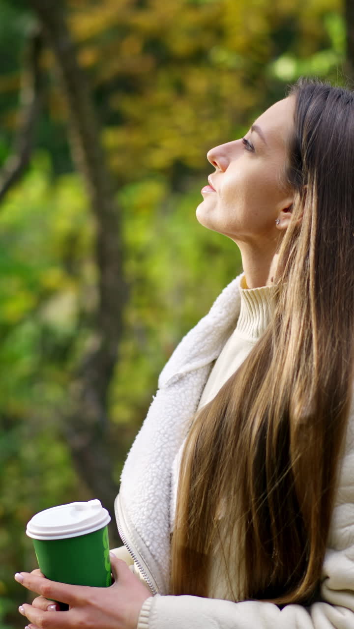 Thoughtful calm long-haired lady spending time in the autumn park. Woman enjoying the rays of sun coming through the trees. Blurred backdrop.