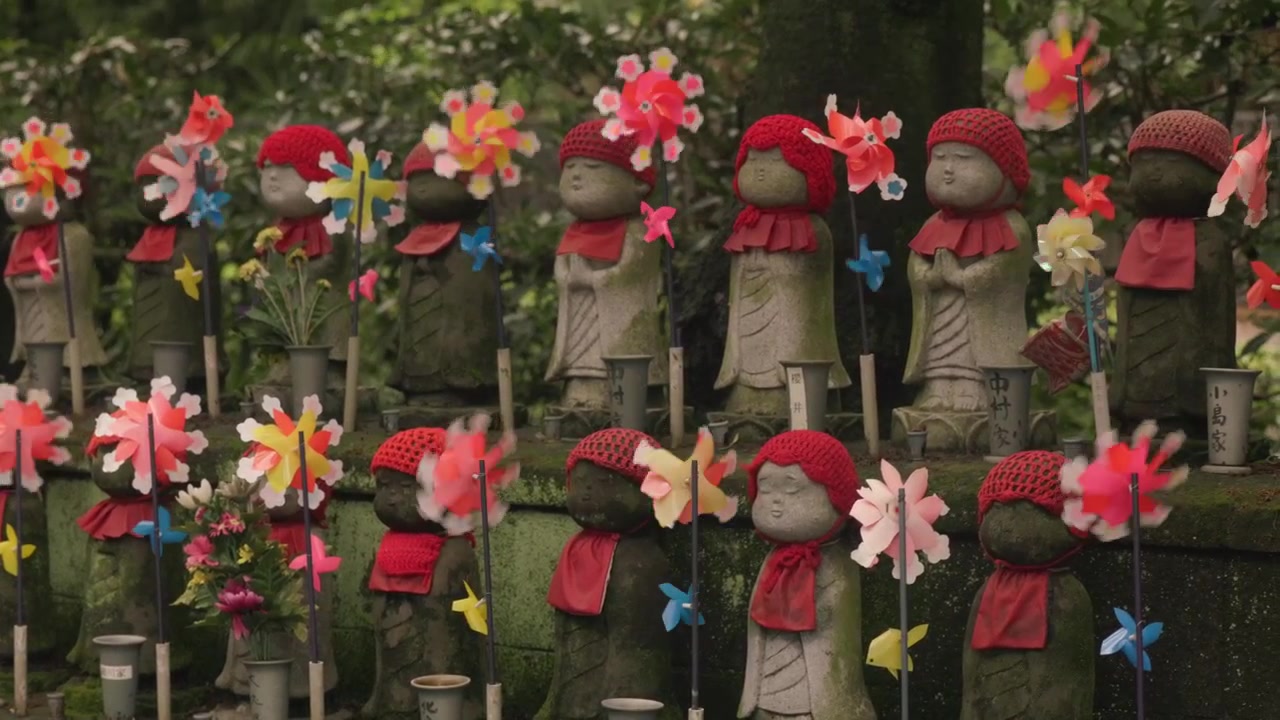 File di statue Jizo adornate con girandole colorate si ergono nel giardino del tempio Zojo-ji a Tokyo, Giappone. Inquadratura statica.
