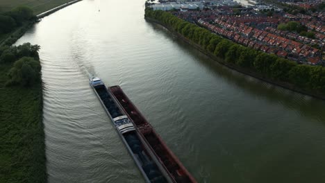 aerial footage of long cargo ship transporting bulk material in barges on river in flat landscape