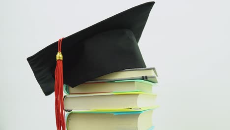 a black square graduate hat with a red tassel lies on a stack of books. the brush is swaying. education concept