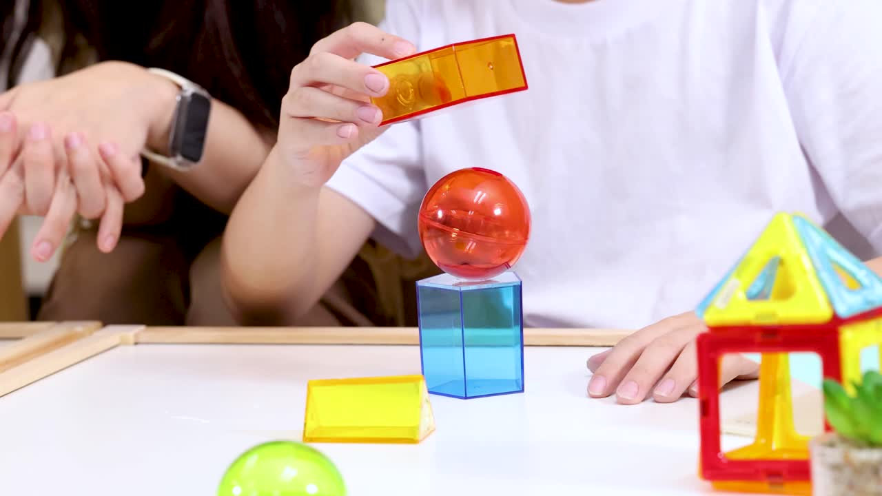 Child builds creative block tower in bright classroom, supervised by smiling teacher, natural lighting