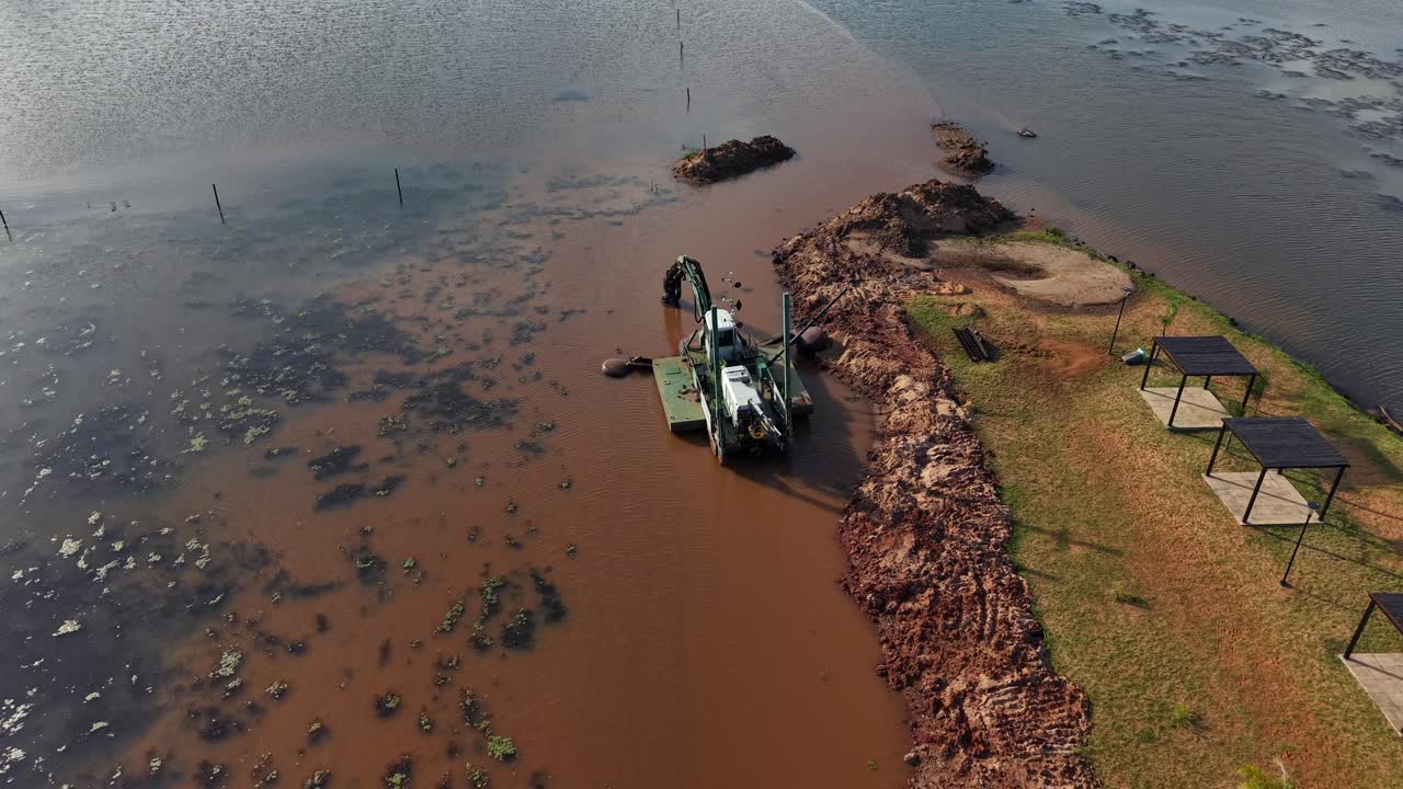 Aerial drone view of an amphibious dredging machine working in muddy water to clear sediment and restore the riverbank