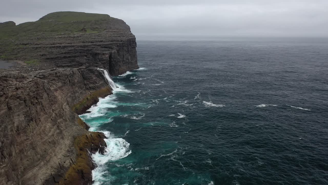 Aerial view along Atlantic sea cliffs and waterfall of Faroe Islands coastline