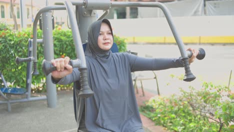 Joven-Musulmana-Con-Hijab-Haciendo-Ejercicio-En-Una-Máquina-De-Hombro-En-Un-Gimnasio-Al-Aire-Libre