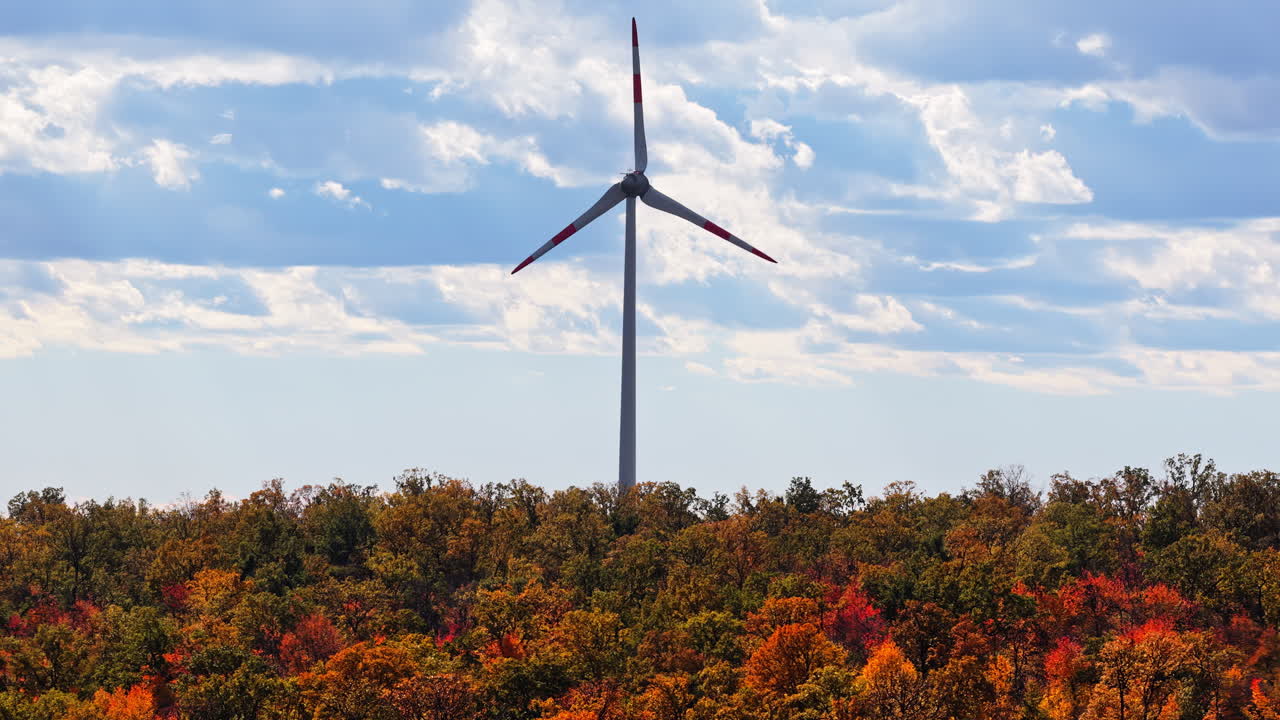 Aerial drone view of a wind turbine rising above colorful autumn forest in Moldova under a bright blue sky