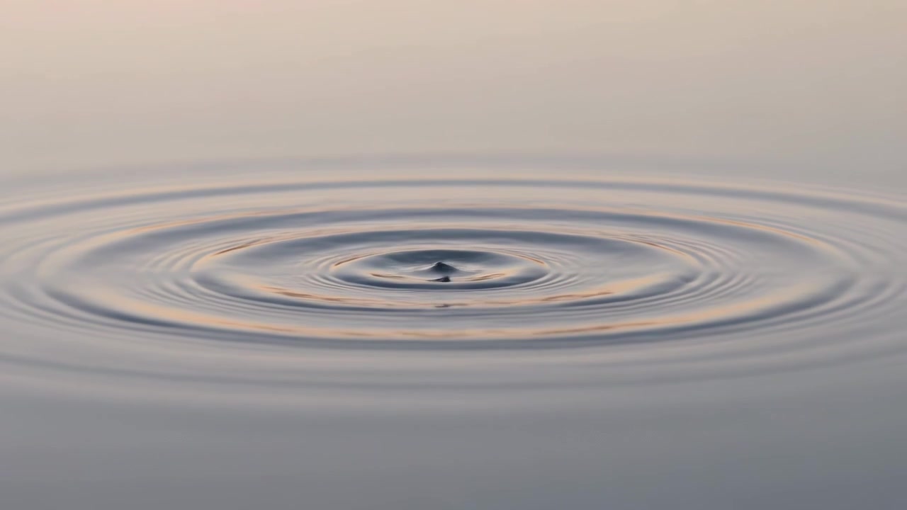 Uno schizzo che colpisce il centro di uno stagno calmo crea increspature concentriche, formando anelli con il riflesso del cielo.