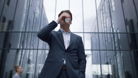 Porträt-Eines-Lächelnden-Geschäftsmannes,-Der-Kaffee-Trinkt-Und-Vor-Einem-Bürogebäude-Aus-Glas-Steht.