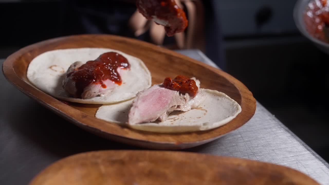 Carne con salsa rossa posta su piccole tortillas all'interno di una ciotola di legno, al rallentatore.