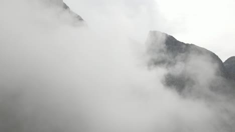 Drone-flying-through-dense-cloudscape-towards-rocky-mountains