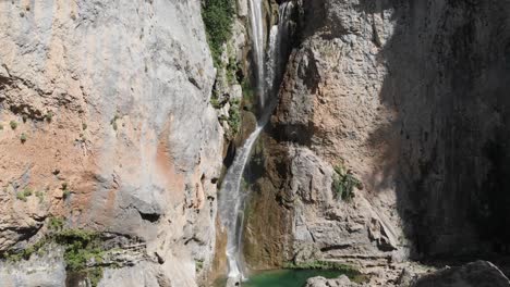 aerial dolly shot of an exotic waterfall in the mountains, as water curving into stone forming a pond