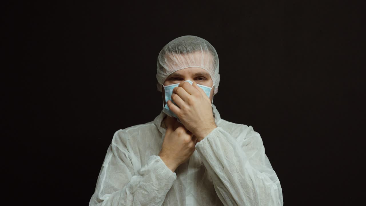 Um homem coloca uma máscara facial médica descartável enquanto veste roupas de proteção e uma touca de cabelo. Conceito de equipamento de proteção individual, normas de higiene e procedimentos de segurança na área médica