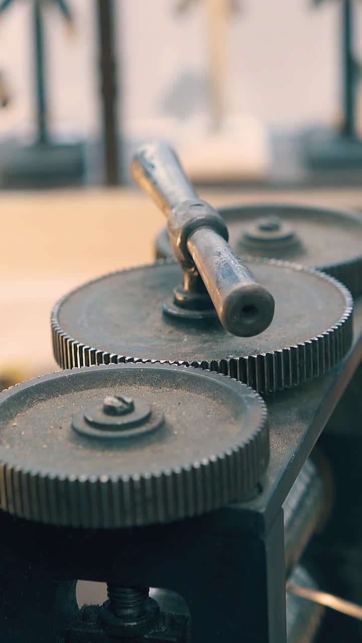 CU shot: goldsmith turns lever on machine tool forge-rolling piece of white metal at workplace in light workshop closeup