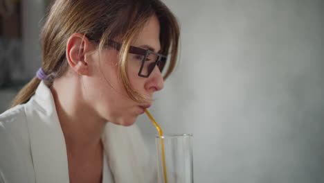 close up of white lady in white top with hair tied back sipping coffee through yellow straw focused on drink with blur background featuring soft light and unclear item