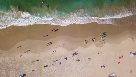 Tourists-roam-across-golden-sand-of-Byron-Bay-beach-Australia-on-sunny-day,-aerial-top-down