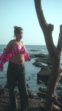 walking along the beach, a woman in a pink checkered cover-up and loose pants enjoys the sea breeze