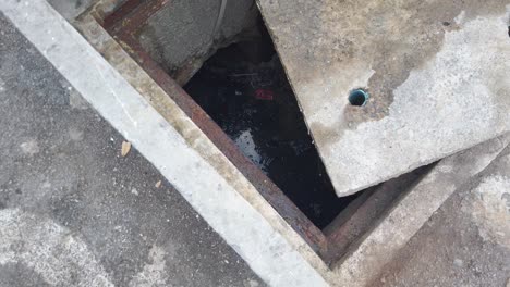 tilt up shot of concrete sewer water drain grate propped open on road