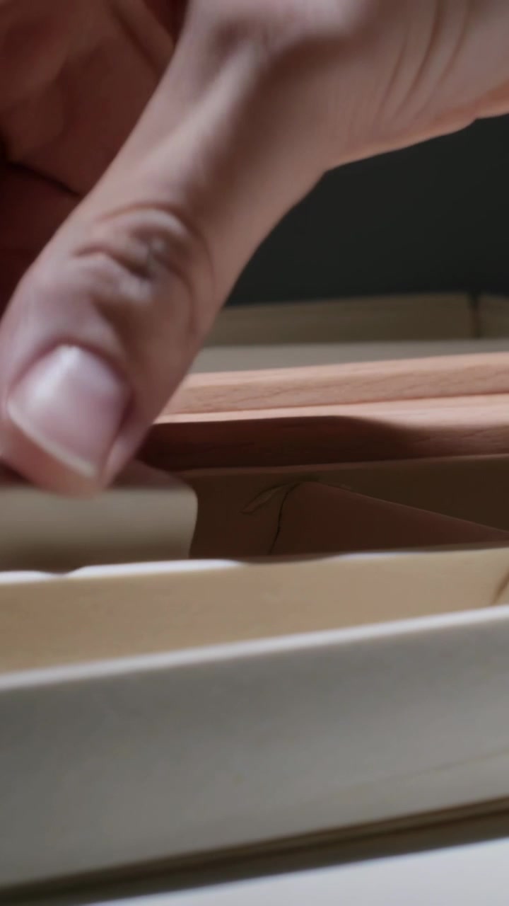 Video verticale: Mano destra che si allunga pizzicando la stecca di legno superiore alla finestra, tirando la plastica intrappolata.