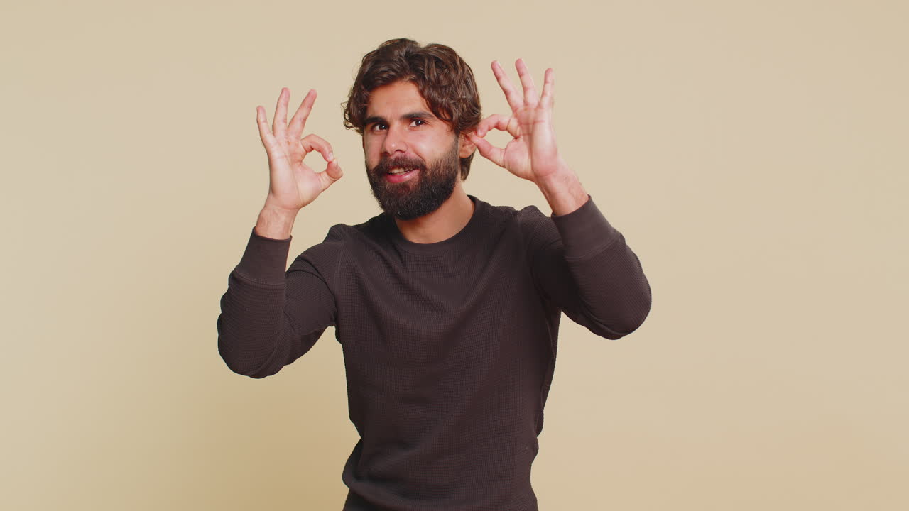 Joyful happy lebanese man in long sleeves looking approvingly at camera against beige background