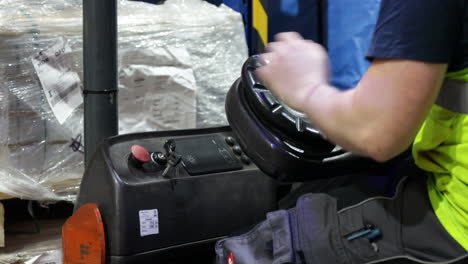 worker wearing yellow protective shirt, caucasian labor starting the electric forklift and drive inside industrial warehouse shipping packaging