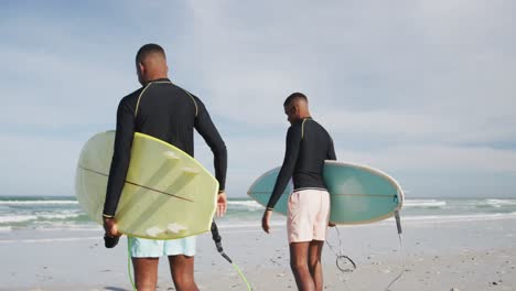 afrikanisch-amerikanische teenager-zwillingsbrüder laufen auf einem strand und tragen surfbretter