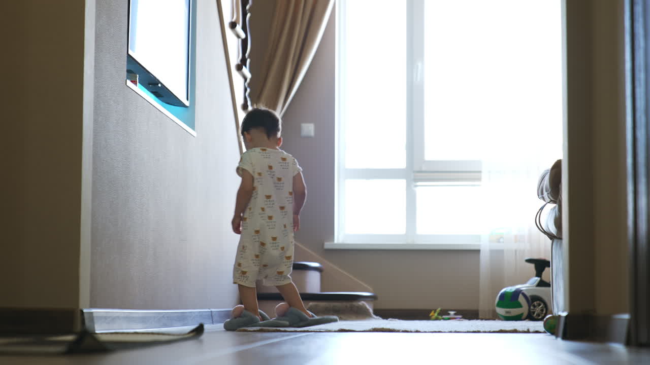 Cute Caucasian boy walks by the room in mom's slippers. Funny child in pajama yawns looking at camera. Low angle view.