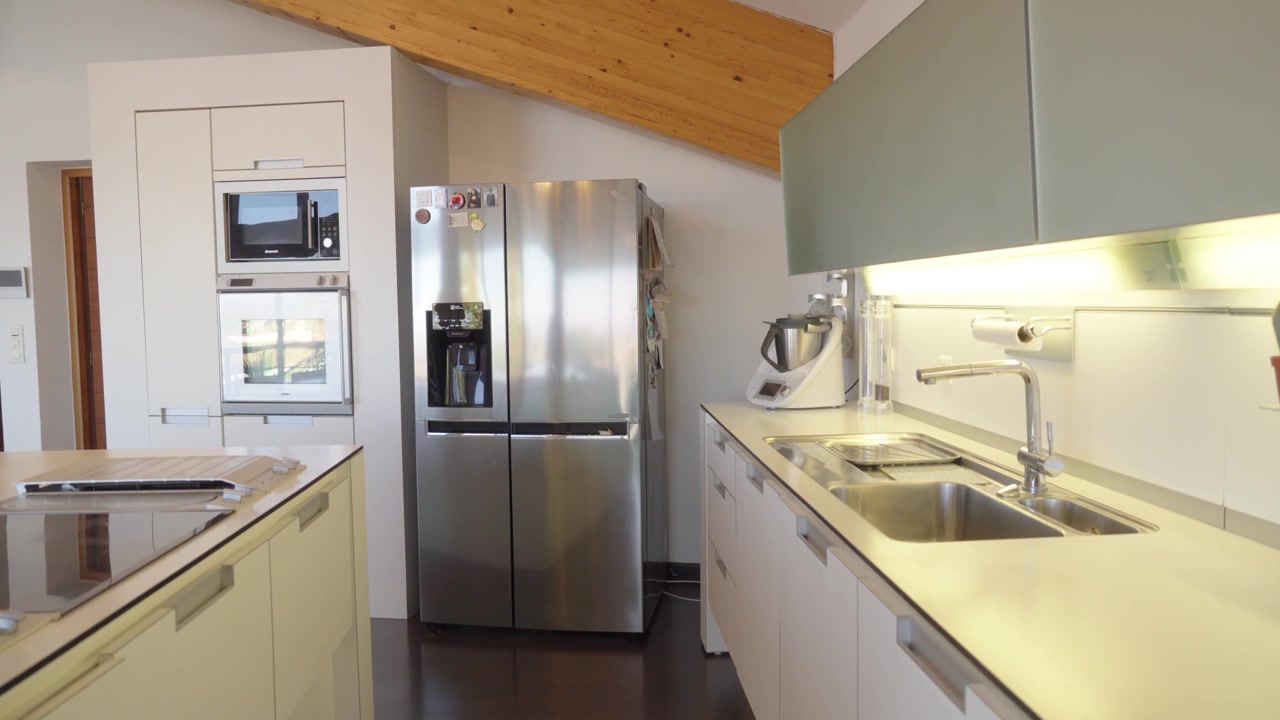 La cámara se desliza por una cocina moderna con gabinetes blancos y electrodomésticos de acero inoxidable