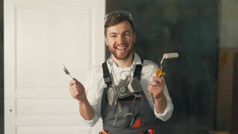 cute man in working uniform of a painter holding a paint roller brush looking at the camera