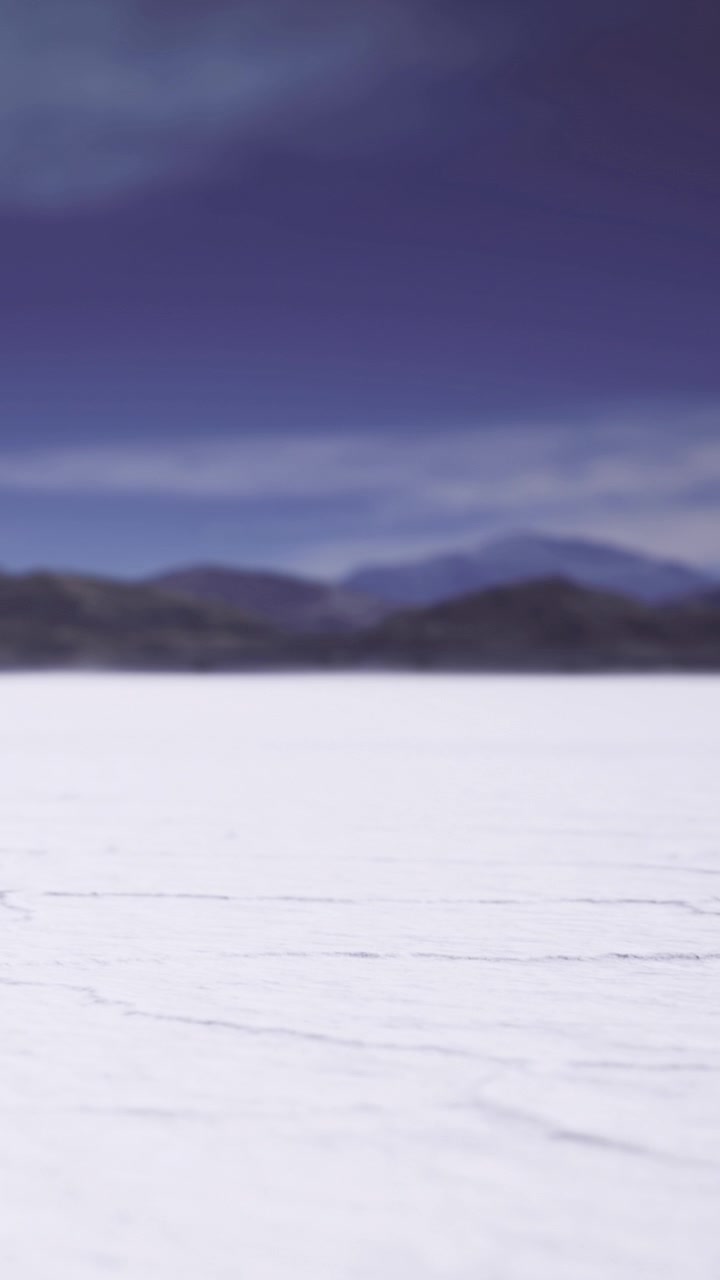 Bright white salt flat under cloudy sky with distant mountains in background
