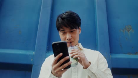 스마트폰 을 사용 하고 밖 에서 음료 를 마시는 젊은 남자