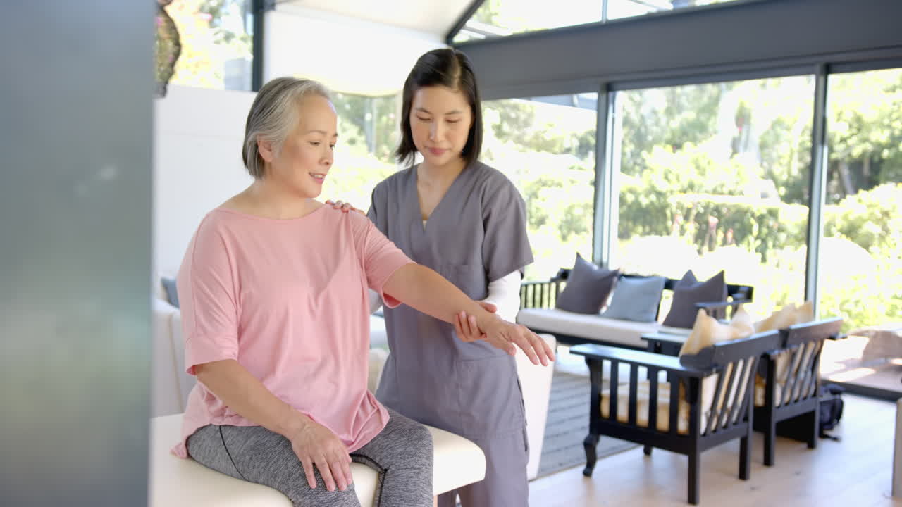 Physiotherapist assisting senior asian woman with arm exercises at home session