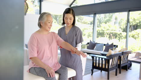 physiotherapist assisting senior asian woman with arm exercises at home session