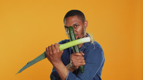 pleased young adult pretending to start a fight with a cucumber and a leek