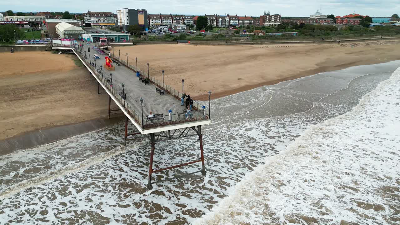 ciudad costera inglesa, fotografiada con un dron, que ofrece un punto de vista aéreo alto que muestra una amplia extensión de playa de arena con un muelle y olas rompientes