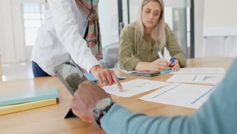 busy diverse business people discussing documents at table with tablet in slow motion