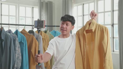 asian man online seller recommending a shirt and recording video by mobile phone while selling clothes at home