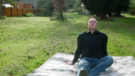 a man relaxing outside sitting in a garden on a mat with eyes closed