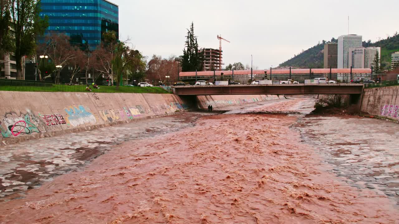 Dolly in drone shot of the flow of the brown Mapocho river and a bridge connecting the city of Santiago Chile, Providencia sector