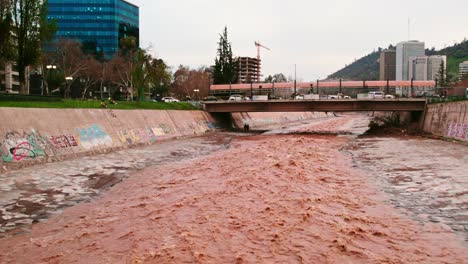 dolly in drone shot of the flow of the brown mapocho river and a bridge connecting the city of santiago chile, providencia sector