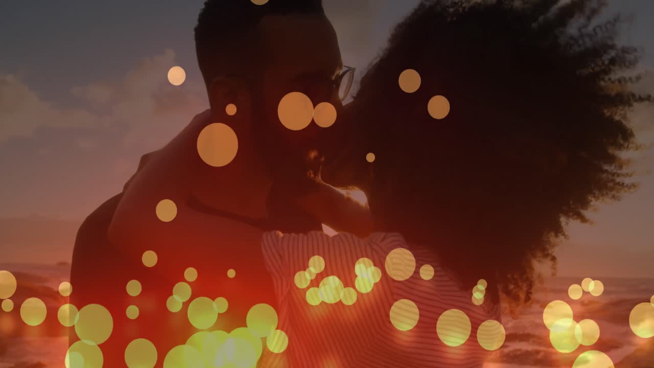 Animation of lens flares over diverse couple hugging and kissing on beach against sea and sky