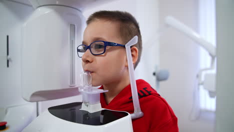 schoolboy in glasses holding plastic piece in his mouth. female doctor speaking to the boy before the procedure of x-ray examination.