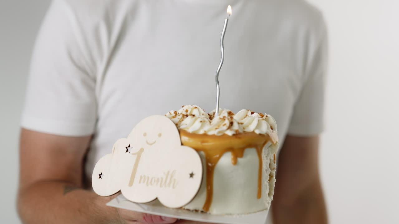 Cropped image of a man holding a cake with 1 month sign on. Man in white shirt light the candle on the cake. Close up.