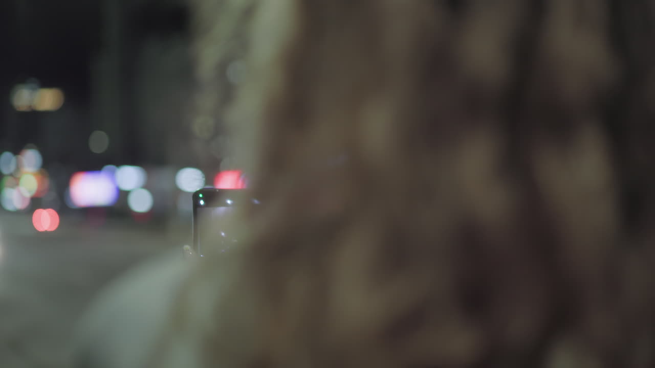 Close up rear view of woman using smartphone to capture night traffic scene, colorful bokeh lights and moving cars creating urban ambiance with glowing streetlight in background
