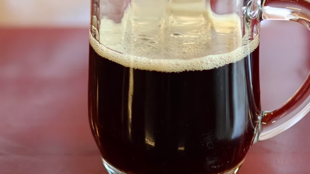 A sequence showing the gradual dissipation of bubbles in a dark soda within a glass mug.